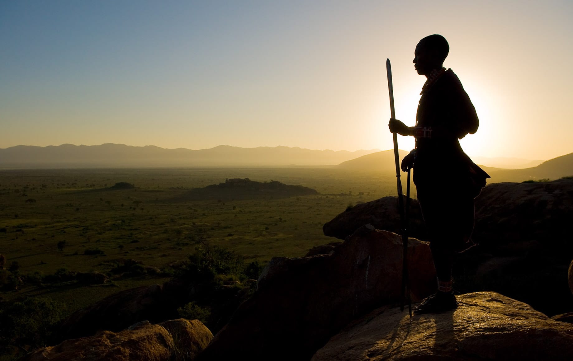 Man standing against setting sun on top of Chyulu Hills