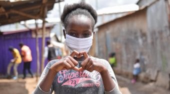 A young girl wearing a mask and making a heart with her hands