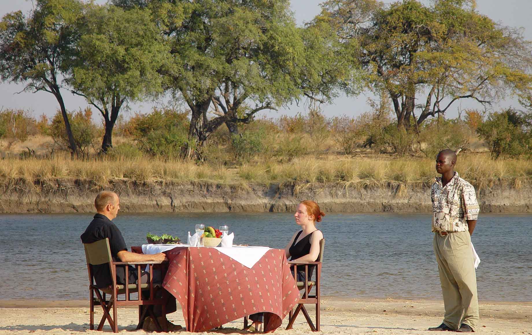 a dinner for two with a waiter near the shore