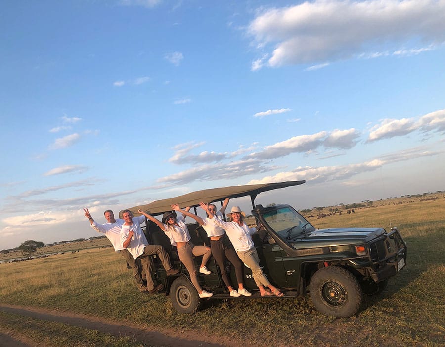 A group of people waving while hanging from the side of a jeep.