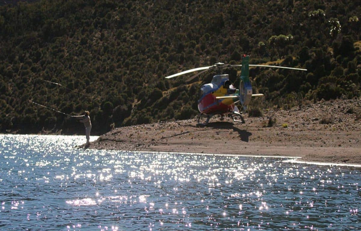 A helicopter over water with a person fishing nearby.